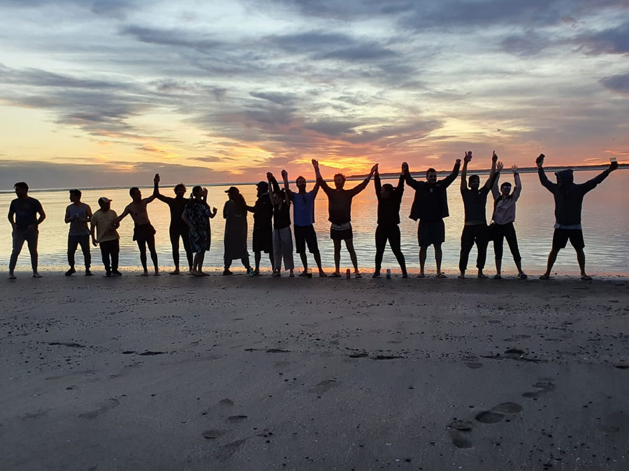Riders celebrating at sunset with arms raised on the sand